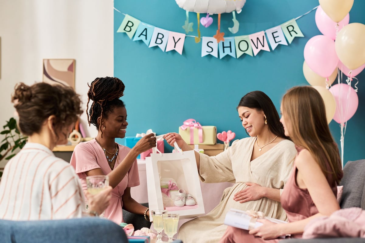 Group of young adult women sitting together celebrating gender reveal party, pregnant woman receiving gift bag