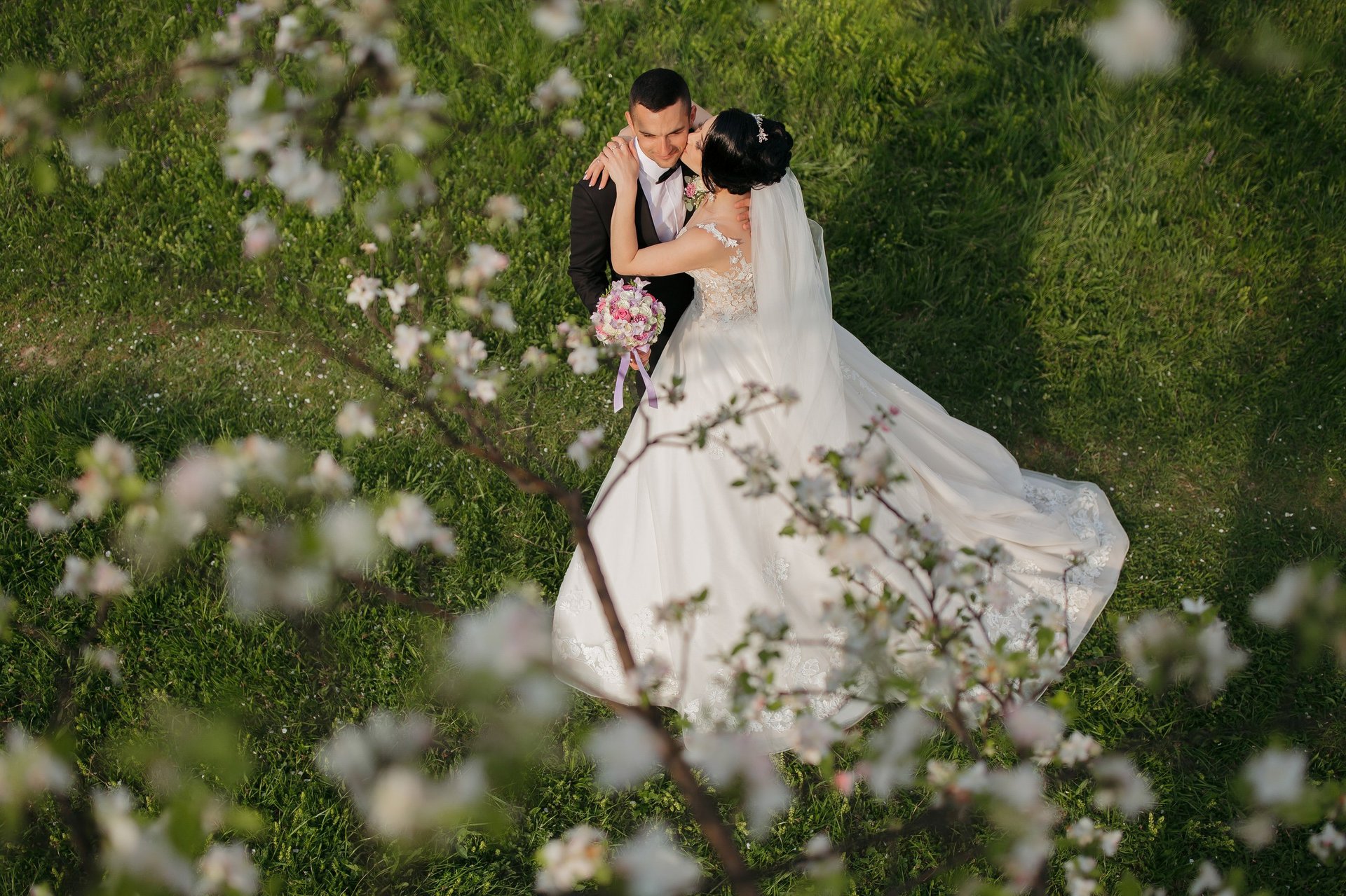 A bride and groom are standing in a field of flowers, with the bride wearing a white dress and the groom wearing a black suit