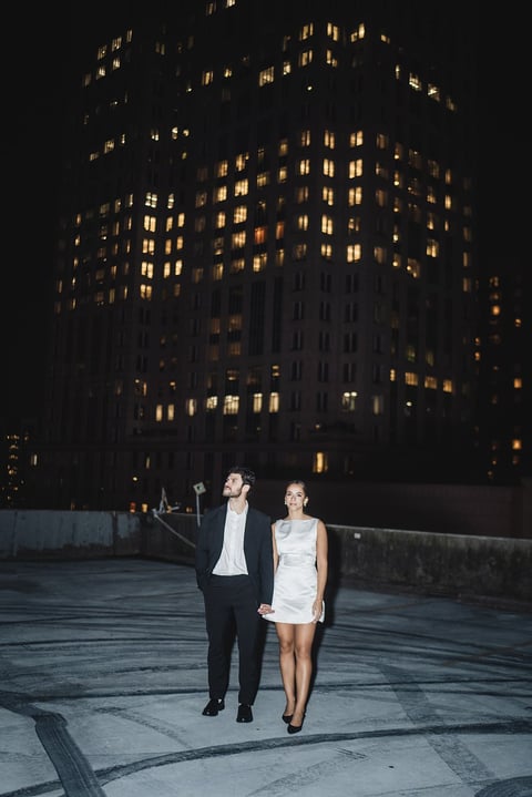 Couple walking hand in hand on urban rooftop at night with illuminated buildings in background