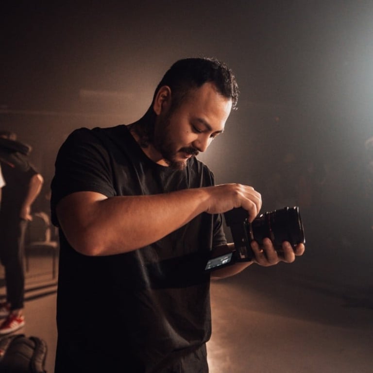 Man in black t-shirt holding and adjusting camera, photographing in atmospheric studio lighting