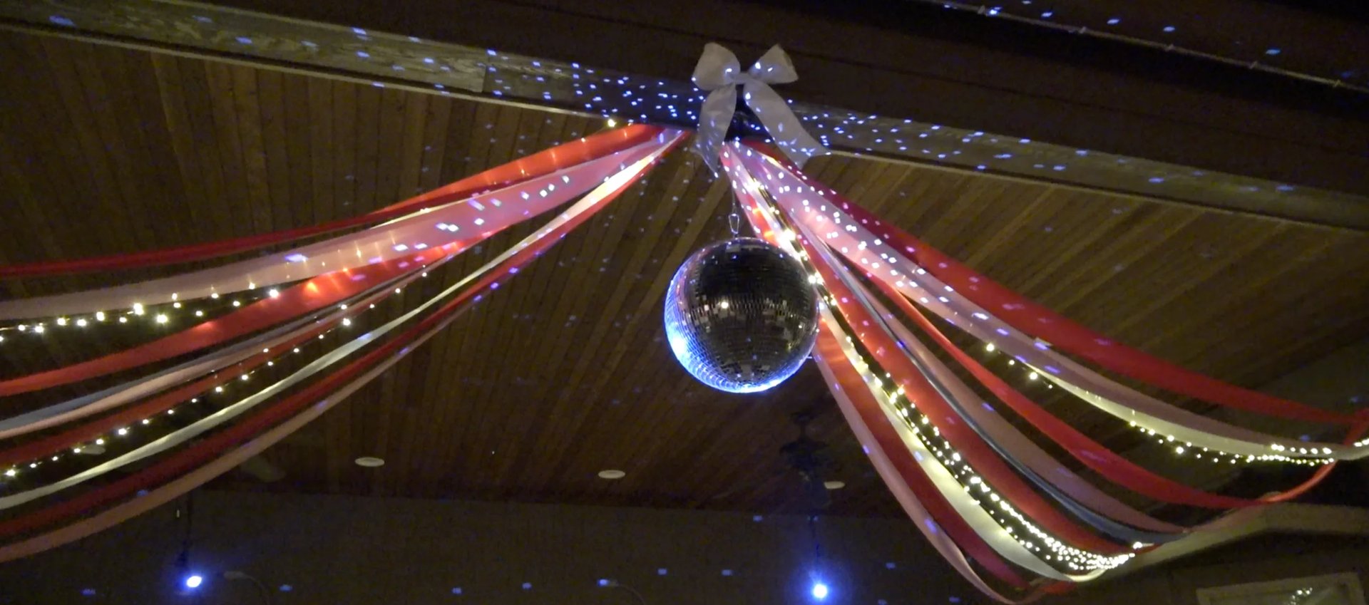 Illuminated fabric drapes and strands converge toward a glowing blue sphere suspended in the center against a dark ceiling