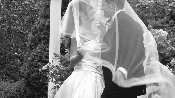 John and Sydney embracing outdoors on their wedding day, brides flowing veil in motion