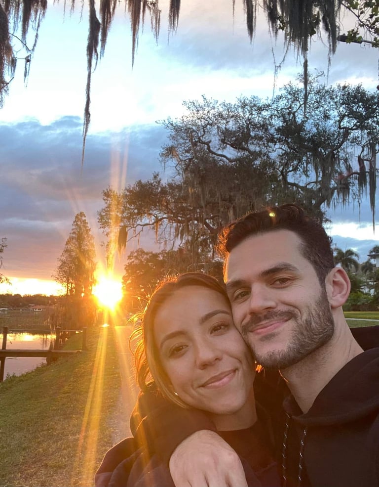 A couple smiling at the camera during sunset with Spanish moss-draped trees and a river in the background