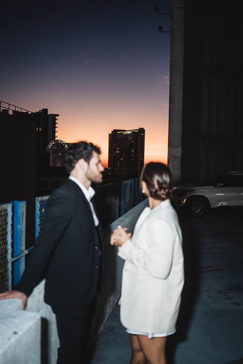 Two people in business attire standing on an urban rooftop at sunset with city skyscrapers in the background