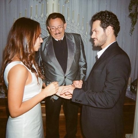 Three people in formal attire at an indoor event, with two men and a woman examining a ring or object in hand