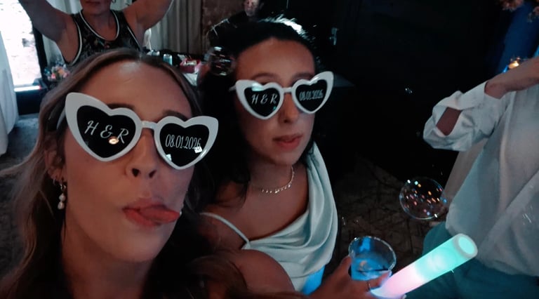 Two women wearing heart-shaped sunglasses at a nighttime party or event, smiling at the camera