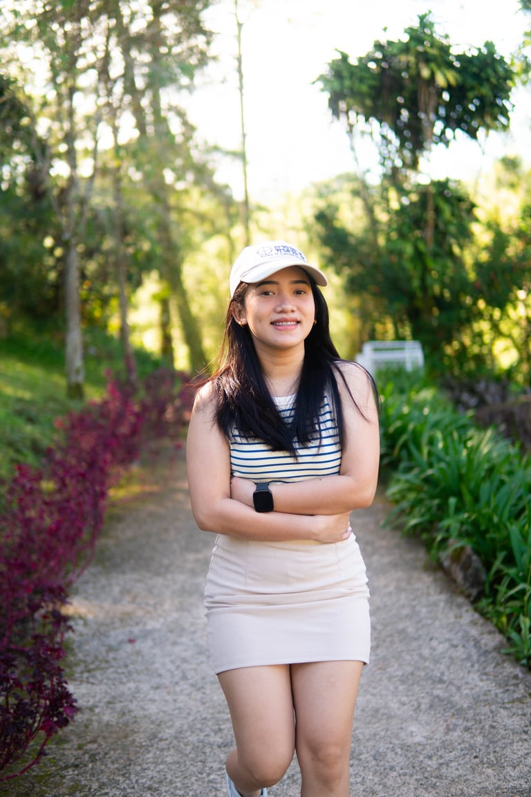 Young woman wearing white cap and striped top standing on garden path lined with green plants and flowers
