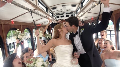 Bride and groom celebrating inside a decorated vintage bus with wedding guests raising glasses in celebration